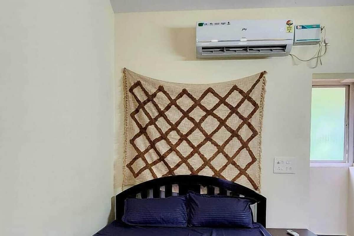 Una cama con cabecera oscura, aire acondicionado fijado a la pared y un tapiz decorativo sobre la cama.