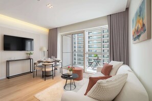 Ein modernes Wohnzimmer mit einer Couch, einem Esstisch, einem an der Wand befestigten Fernseher und großen Fenstern mit Blick auf die Stadt.