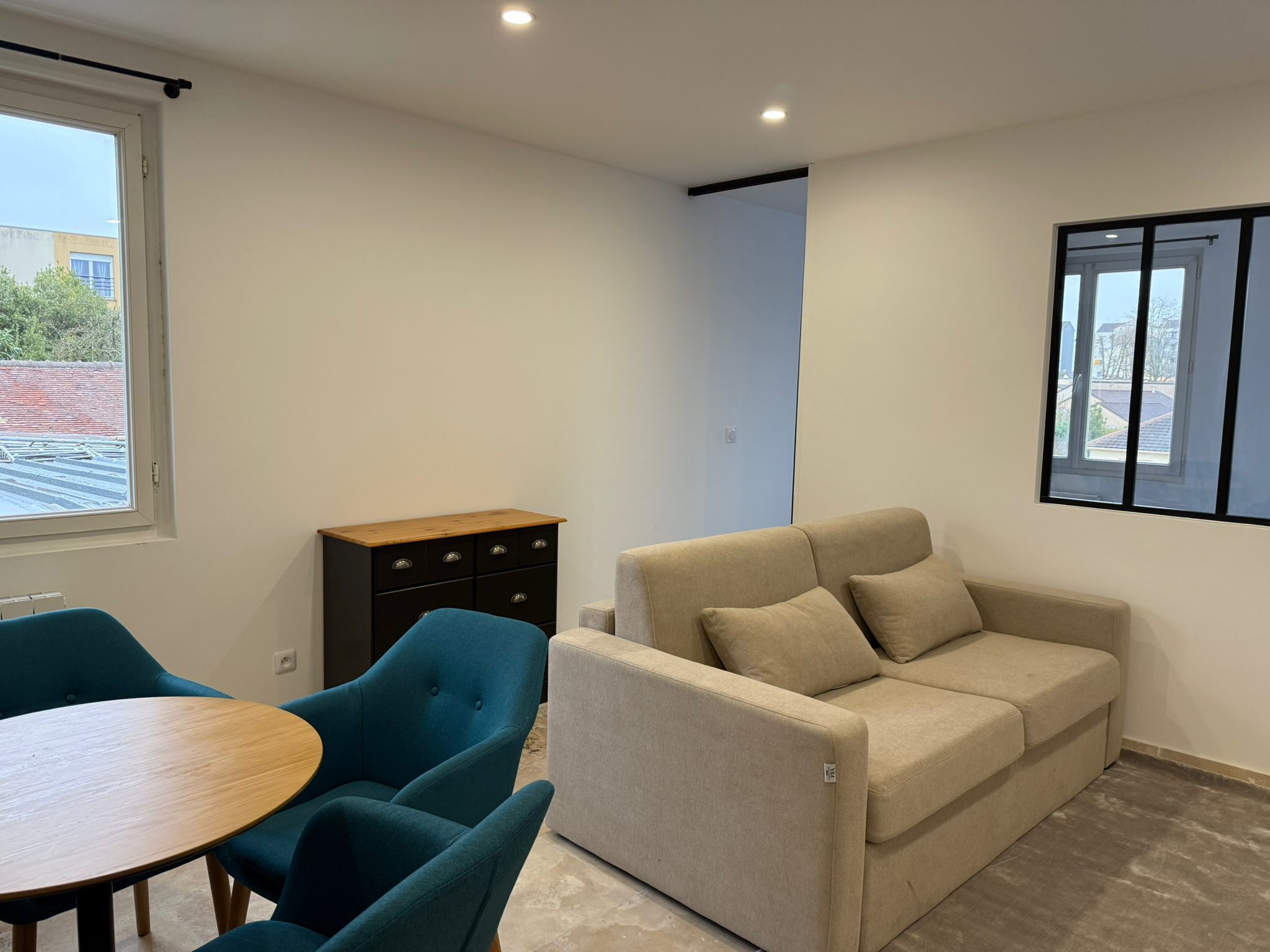 A modern living room with a beige sofa, teal chairs, a wooden table, and a black dresser.