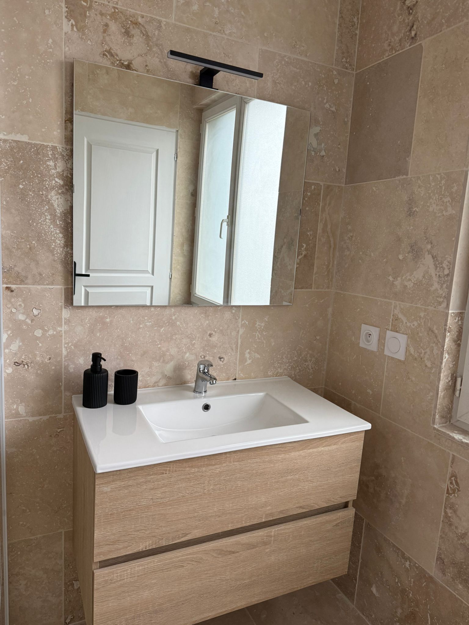 A bathroom with a white sink, a mirror above it, and beige tiled walls.