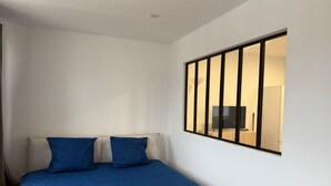 Un dormitori amb un llit, dues almoines, una finestra amb persianes i una televisió al reflex.