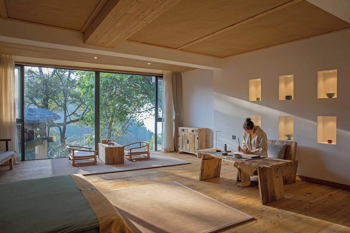 A spacious room with a large sliding glass door leading to a balcony, wooden furniture, and built-in wall sconces.