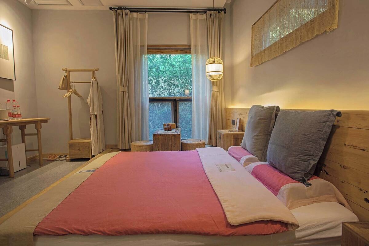 A bedroom with a large bed, a wooden headboard, a bedside table, a hanging lamp, and a window with curtains.