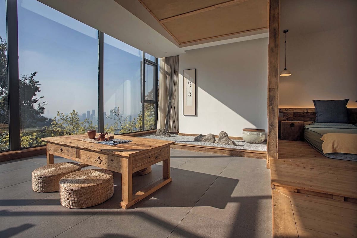 A modern interior with a wooden dining table, woven poufs, and a minimalist design.