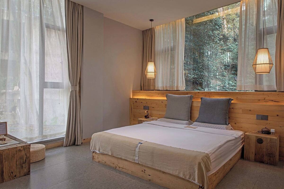 A bedroom with a large bed, wooden headboard, two bedside tables, and a window with curtains.
