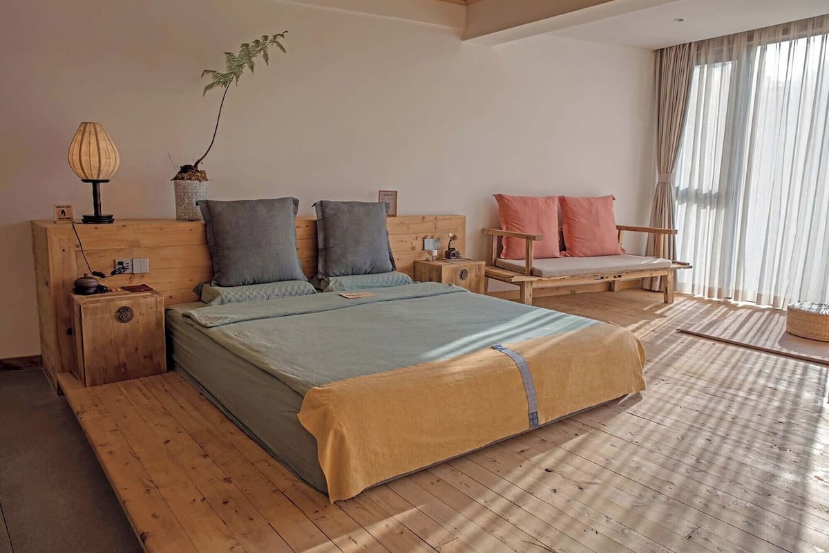 A bedroom with a wooden bed, a bedside table, a nightstand, a chair, and a window with curtains.