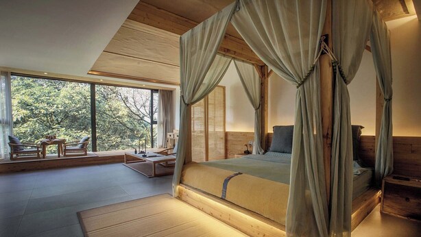 Un dormitorio amplio con una cama grande, un espacio para sentarse con una mesa y sillas, y vistas al exterior.