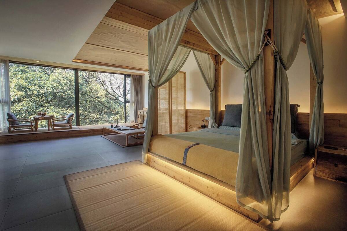 A spacious bedroom with a large bed, a sitting area with a table and chairs, and a view of the outdoors.