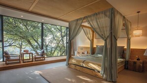 Un dormitorio con una cama con dosel, ventanas amplias y vistas a árboles.