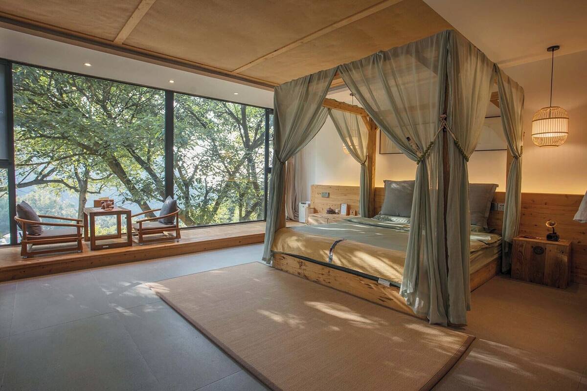 A bedroom with a four-poster bed, large windows, and a view of trees.