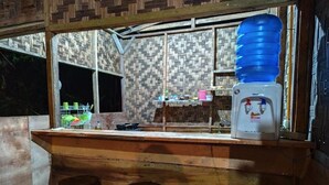 Zona de bar con un dispensador grande de agua, taburetes de madera y una pared estampada al fondo.