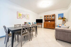 A living room with a dining table, chairs, a sofa, a TV, and a wooden cabinet. - Spacious Apartment in Alghero (Alghero)
