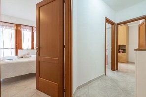 A hotel room with a bed, a wooden door, and a hallway leading to another room. - Spacious Apartment in Alghero (Alghero)