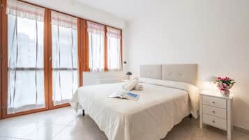 Um quarto com uma cama grande, uma mesa de cabeceira com abajur e uma janela com cortinas.