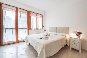 Ein Schlafzimmer mit einem großen Bett, einem Nachttisch mit Lampe und einem Fenster mit Vorhängen.