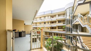 Ein mehrstöckiges Gebäude mit Balkonen, einem zentralen Innenhof mit Pflanzen und einer Treppe.