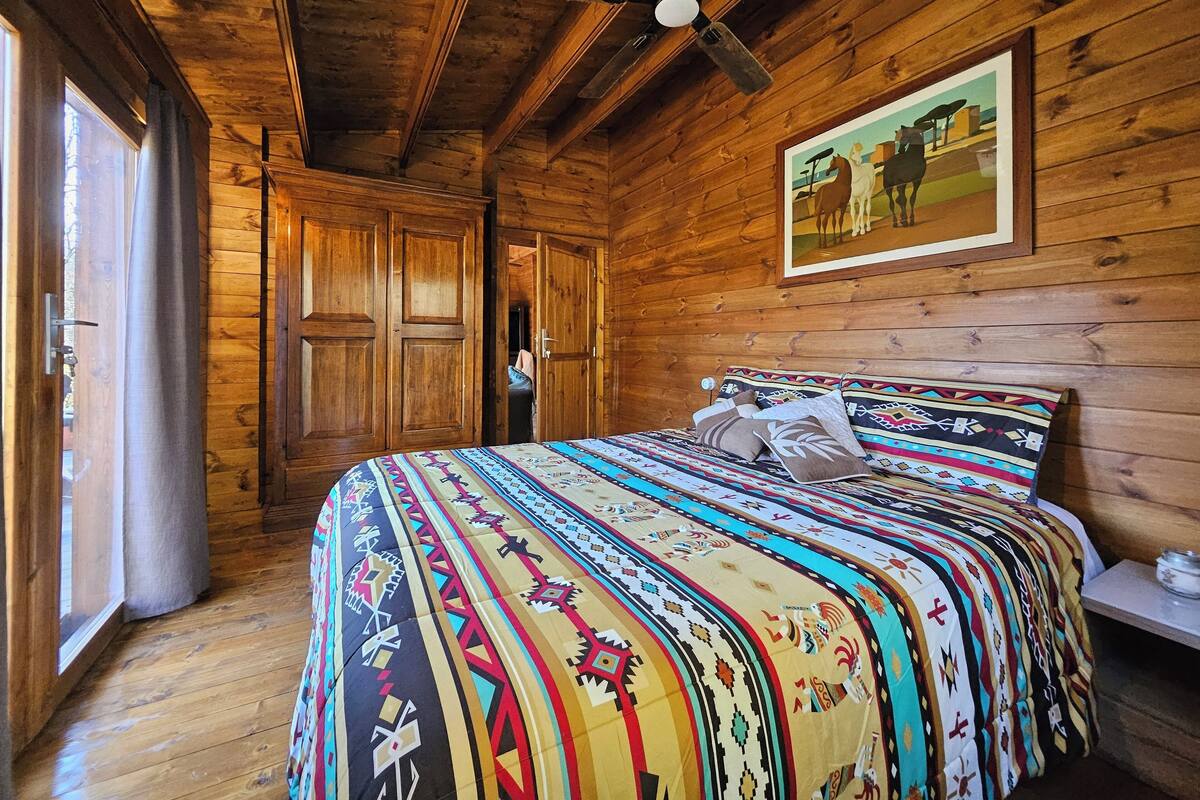 A wooden cabin bedroom with a bed, a ceiling fan, and a painting on the wall.