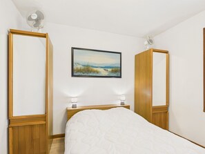 Ein Schlafzimmer mit einem Bett, einem Nachttisch, einem Gemälde und zwei Wandventilatoren.