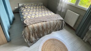 A bedroom with a bed, a window with curtains, a radiator, and a woven rug on the floor.
