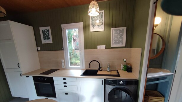 A compact kitchen with a dishwasher, washing machine, and a sink. There is a window with a view of greenery outside.