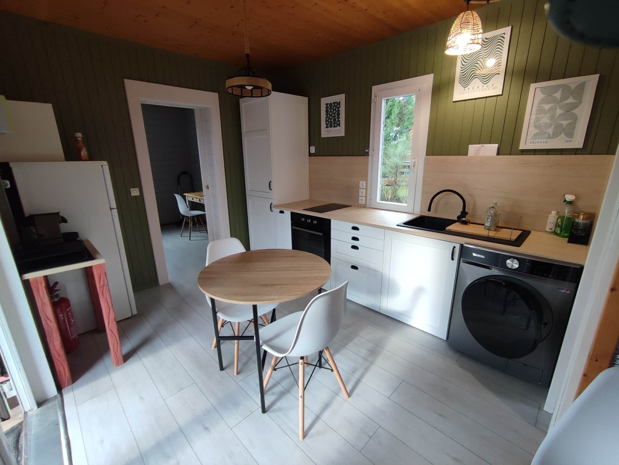 Kompakti keittiö, jossa on ruokapöytä, tuolit, pesukone ja ikkuna.