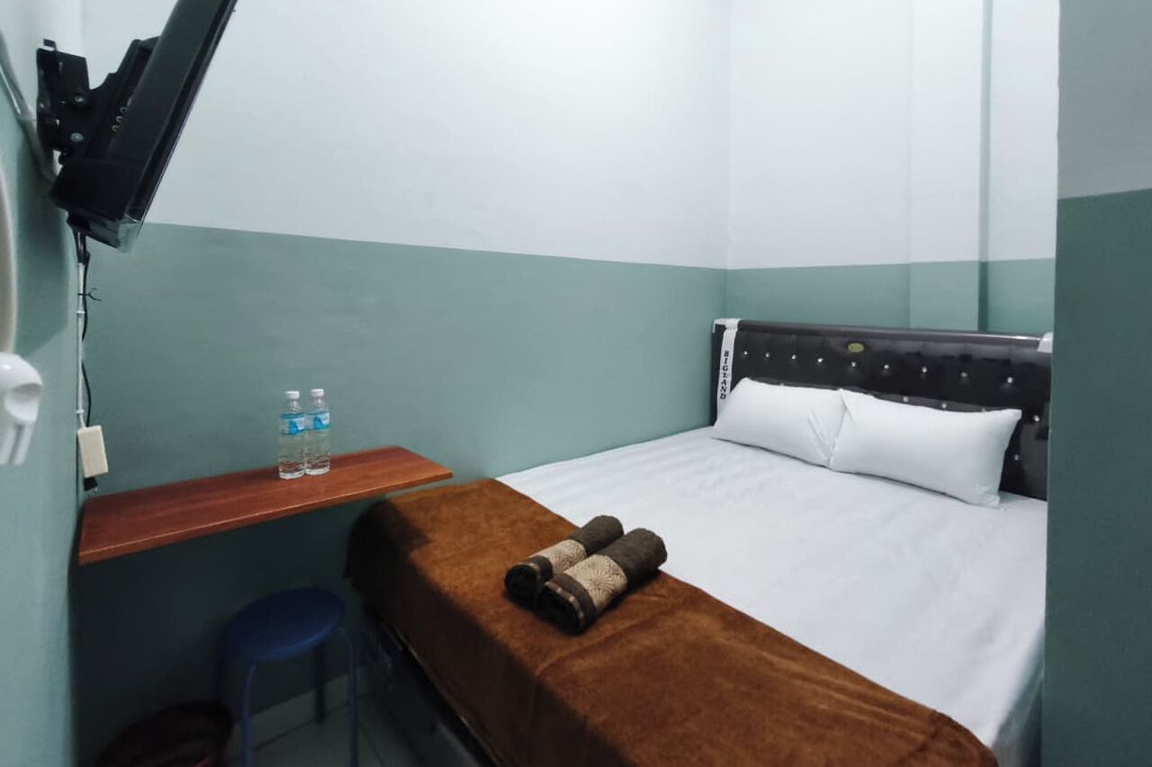 A hotel room with a bed, a wooden desk, a blue chair, and a TV mounted on the wall.