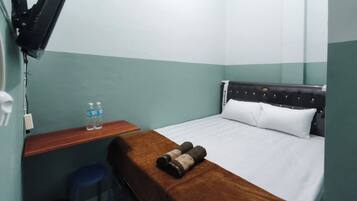A hotel room with a bed, a wooden desk, a blue chair, and a TV mounted on the wall.