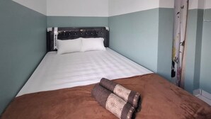 Una cama bien hecha con cubierta marrón y almohadones decorativos, cabecera con el nombre de una marca y cortina con estampado de mariposas.