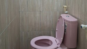 Un baño con inodoro rosa, un bidé de pared y un desagüe en el suelo.