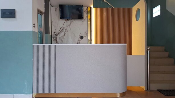 Un mostrador de recepción con una pared de mármol, un televisor montado encima y una escalera con paneles de madera a la derecha.