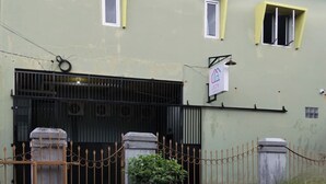 Una entrada protegida con cerca metálica, un poste de concreto y un arbusto pequeño al frente.
