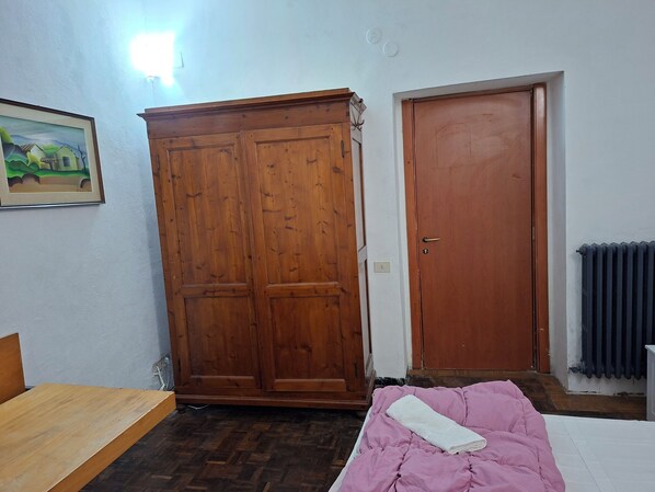 A room with a wooden wardrobe, a closed door, a radiator, and a bed with a pink blanket. - Bed in Siena (Siena)