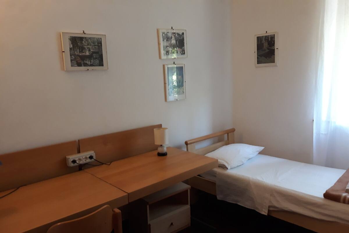 A room with a wooden desk, a chair, a bed, and three framed pictures on the wall.