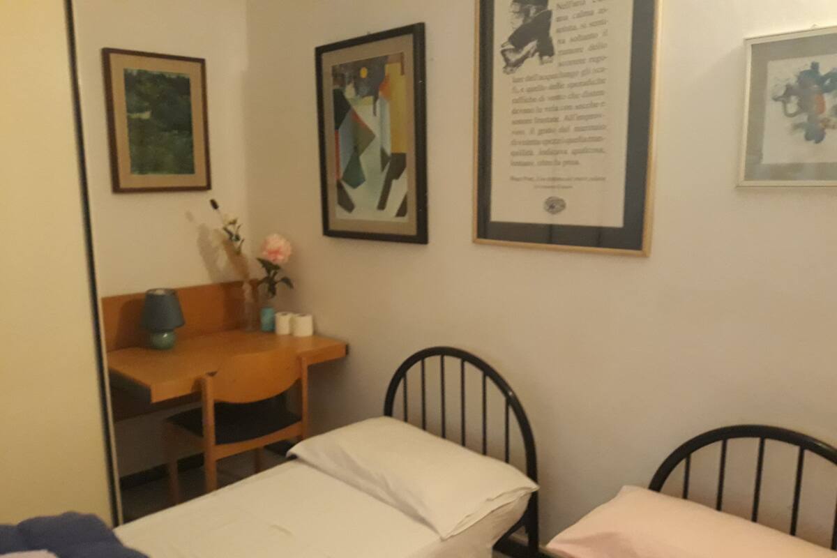 A room with two beds, a desk, and framed artworks on the wall.