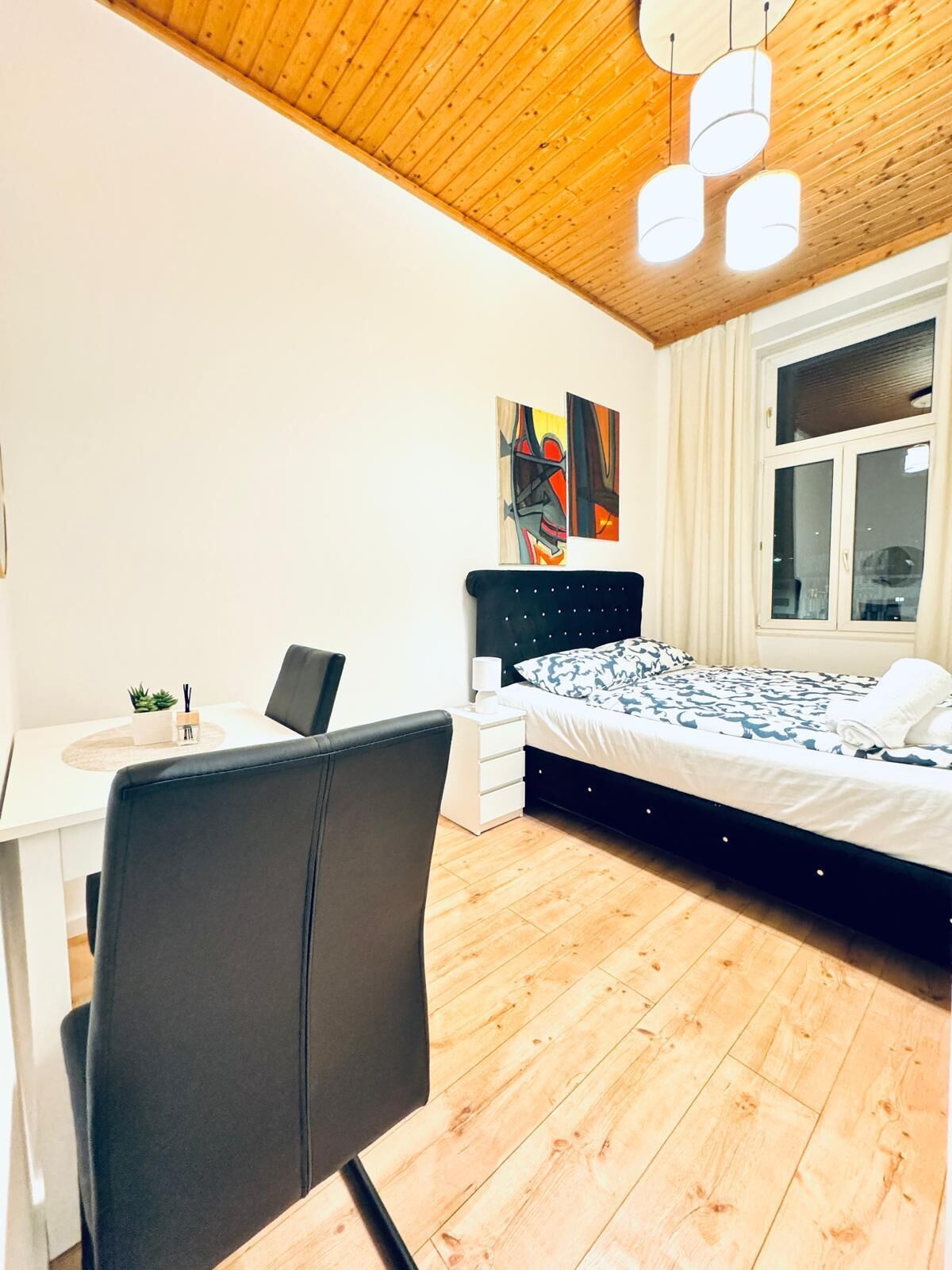 Ein modernes Schlafzimmer mit Holzboden, einem Bett mit gemusterten Betttextilien, einem Schreibtisch mit Stuhl und Bildern an der Wand.
