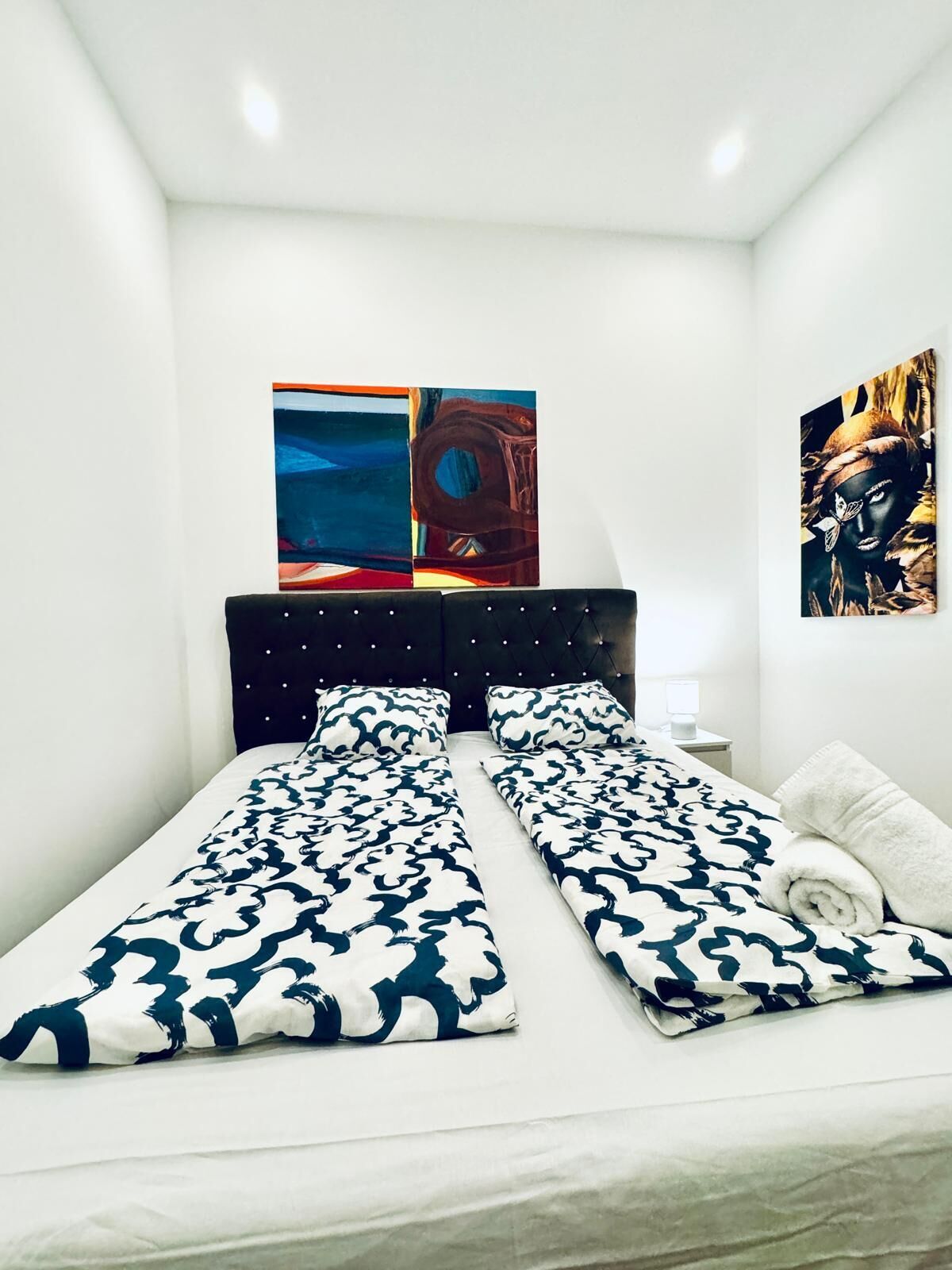 Un dormitorio con dos camas individuales, cabecera oscura y dos cuadros en la pared.