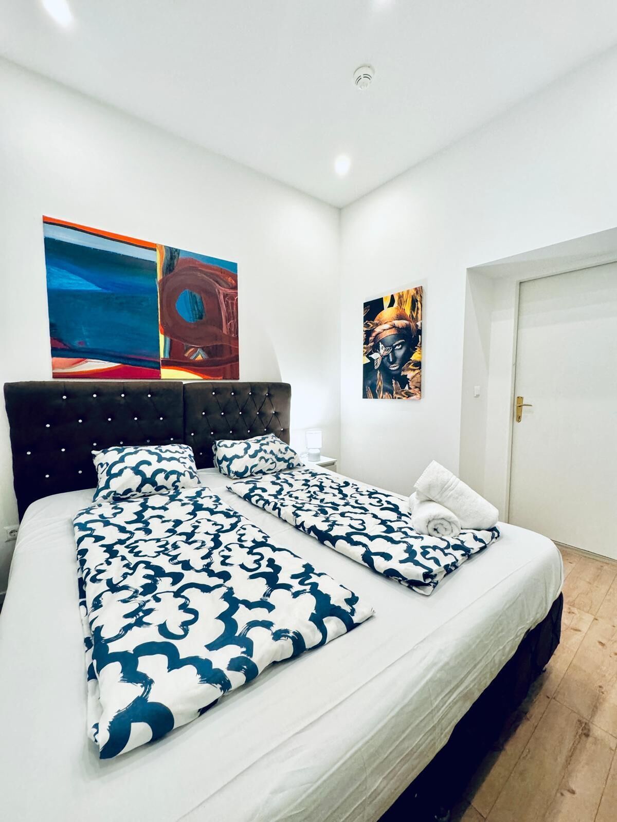 A modern bedroom with a large bed, two side tables, and artwork on the walls.