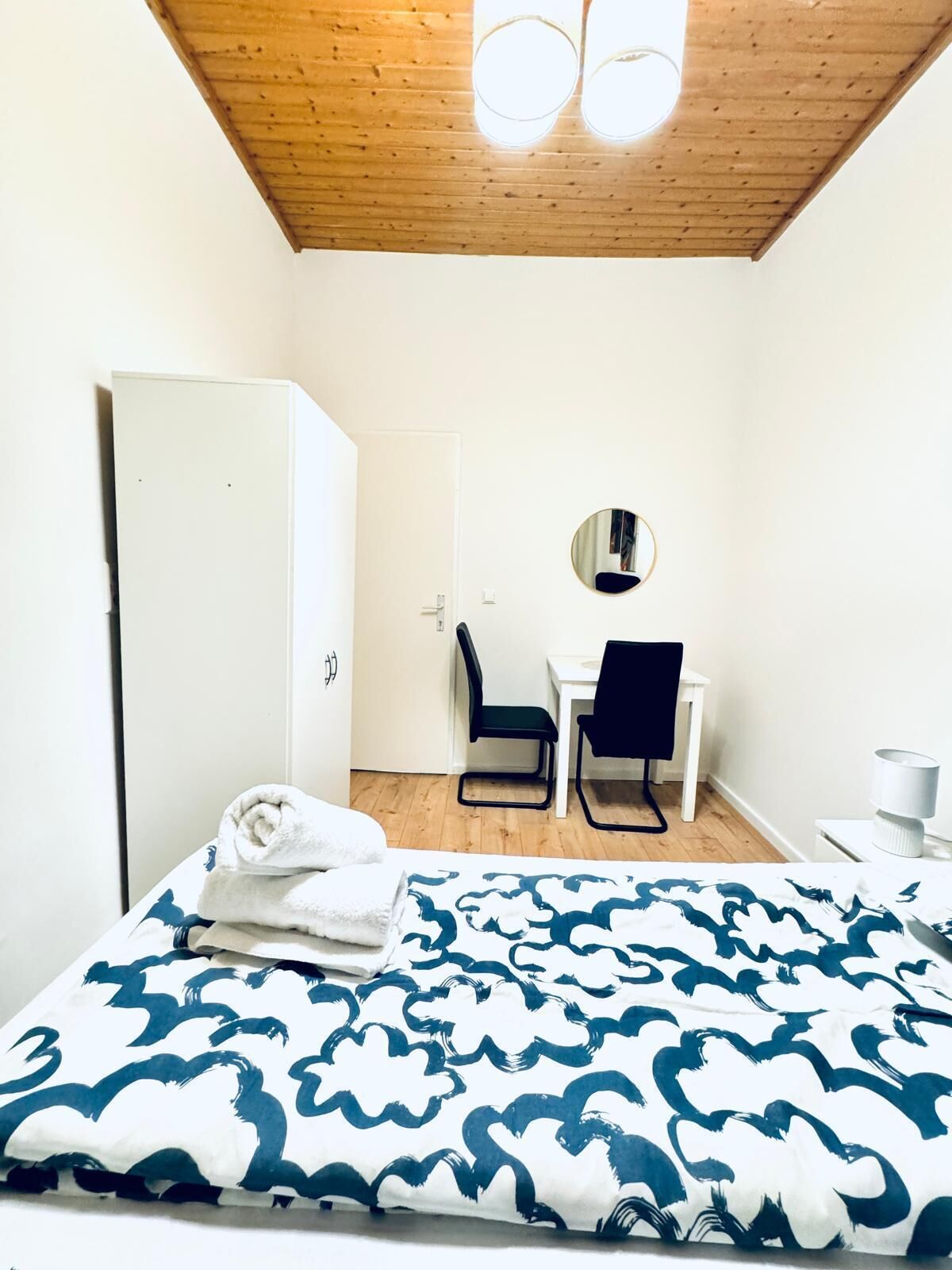 A small, tidy room with a bed, a desk, a chair, and a wardrobe.