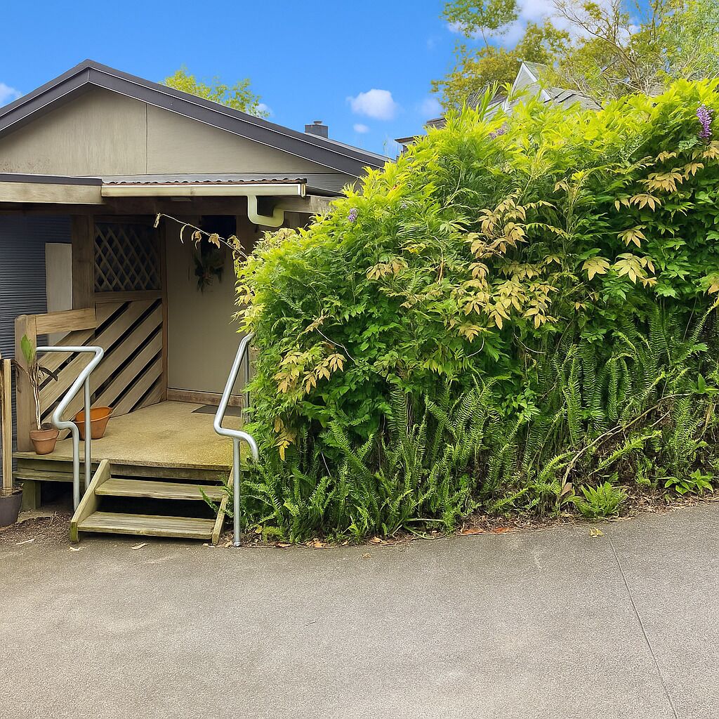 Une maison avec un escalier en bois menant à un porche, le tout entouré d’un feuillage verdoyant et luxuriant.