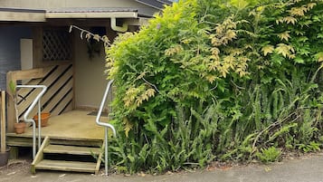 Une maison avec un escalier en bois menant à un porche, le tout entouré d’un feuillage verdoyant et luxuriant.