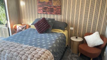 A bedroom with a bed, a chair, a small table, and a wall with vertical lines.