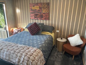 A bedroom with a bed, a chair, a small table, and a wall with vertical lines.