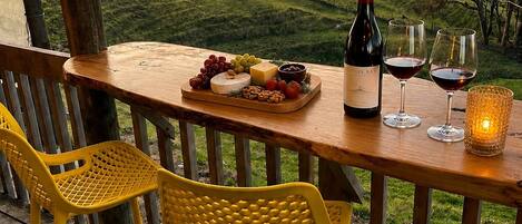 Une terrasse en bois avec une table dressée pour un repas, agrémentée d’une bouteille de vin, de verres et d’un plateau de fruits.