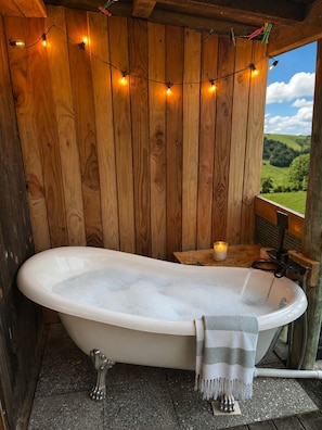 A wooden cabin bathroom with a freestanding bathtub, string lights, and a view of the countryside. - Swallows Nest Cottage -self contained with amazing views and outdoor bath. (Waiatarua)