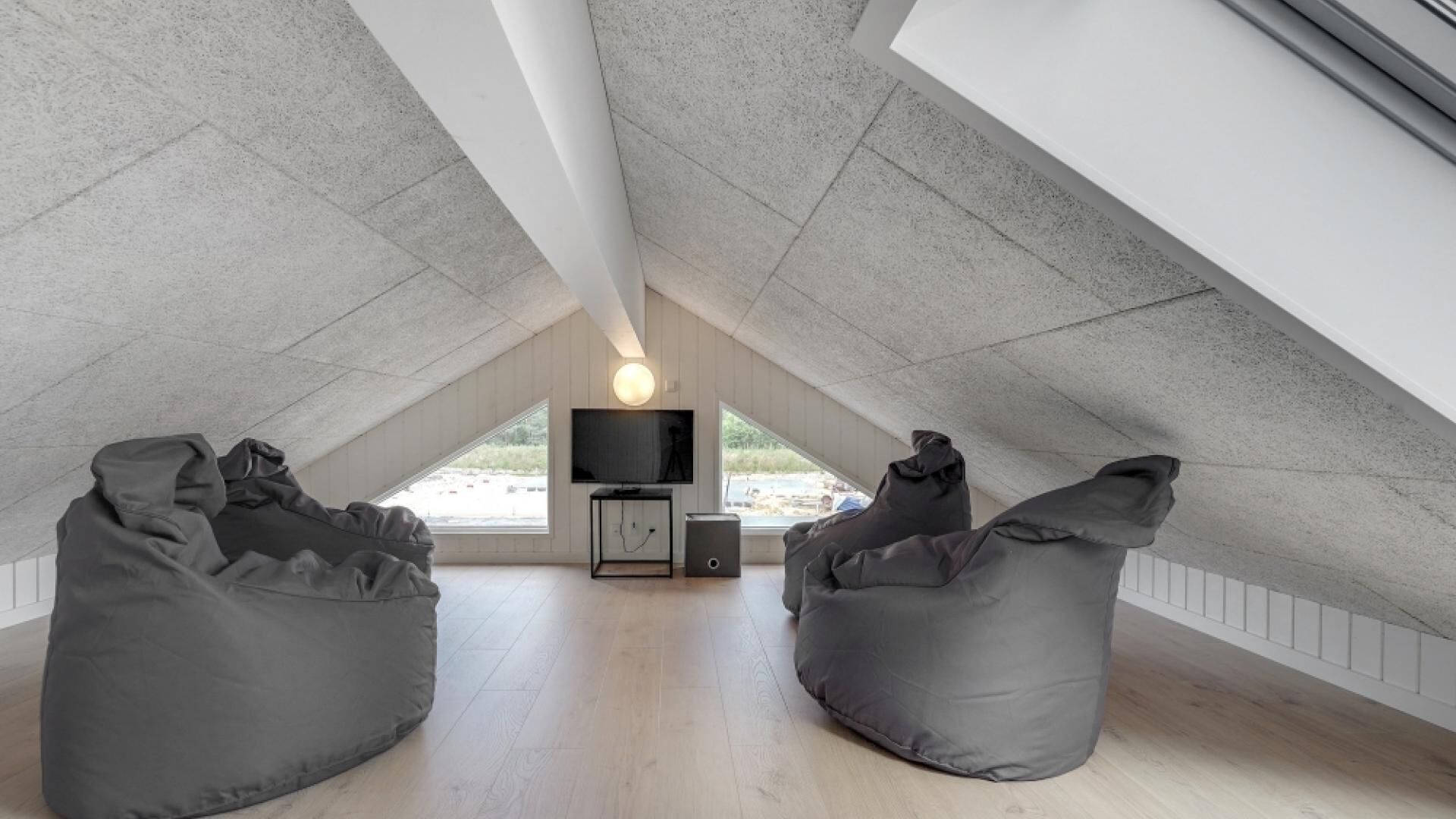 Une chambre mansardée avec un plafond en pente, deux fauteuils poire, une télévision et une petite table.