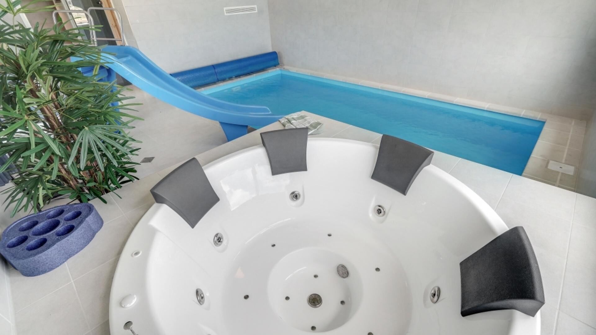 Un jacuzzi con un tobogán azul, rodeado de piso de baldosas y una planta en maceta.