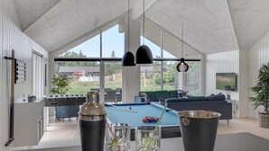Ein geräumiger Wohnbereich mit Billardtisch, Sitzgelegenheiten und großen Fenstern mit Blick ins Freie.