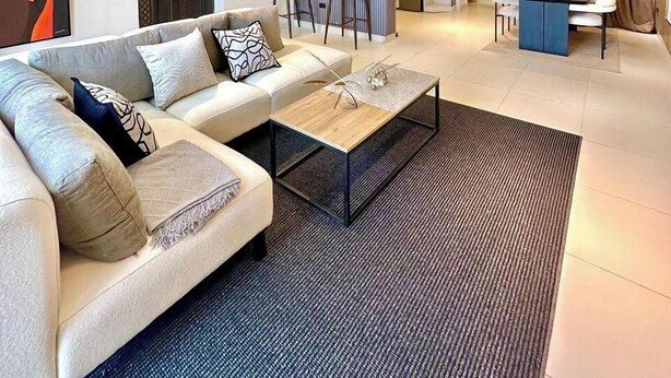 A modern living room with a sofa, coffee table, and a kitchen area in the background. - Deluxe Haven Apartment (Lekki)