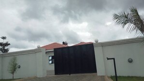 A gated entrance to a building with a red-tiled roof, a paved driveway, and a palm tree to the right. - Boutique Ensuite Room Mineheart Hotel, Masvingo (Masvingo)