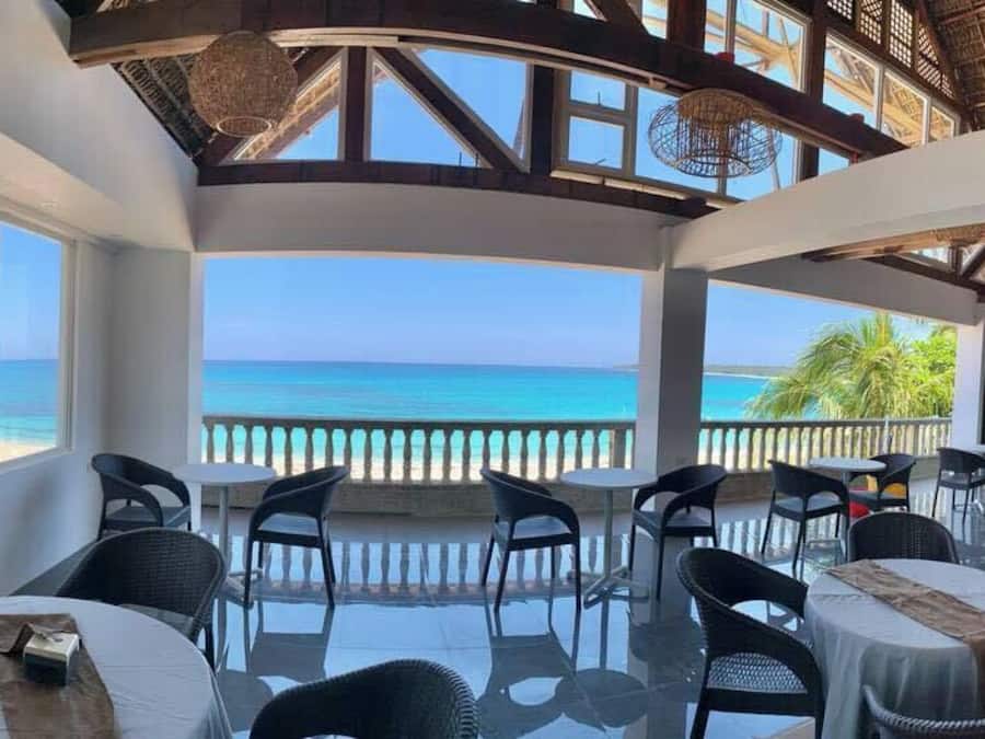 A covered outdoor seating area with tables and chairs, overlooking a beach and ocean.
